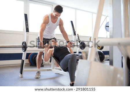 Athletic Young Gym Instructor Guy Supporting a Fit Woman Student in Lifting Barbell Exercise Inside the Gym
