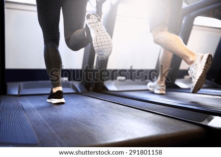 Toned Legs of Healthy Young Couple Exercising on Treadmill Device Inside Fitness Gym.