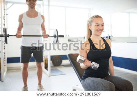 Happy Young Fit Couple Lifting Barbells While Looking at theirselves on the Mirror Inside the Gym