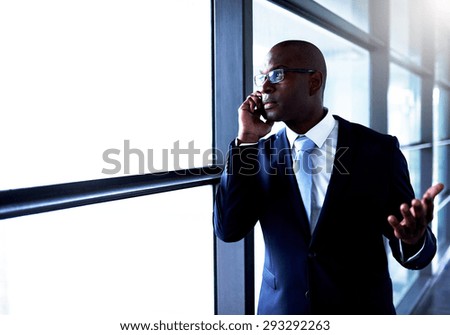 Young Black American Businessman Talking to Someone on Mobile Phone Beside the Glass Window Inside the Building.