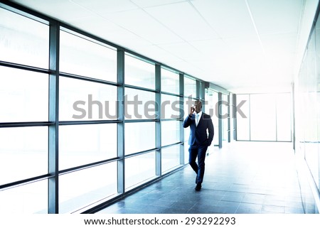 African American Business Talking to Someone on Mobile Phone While Walking at the Walkway Inside a Building