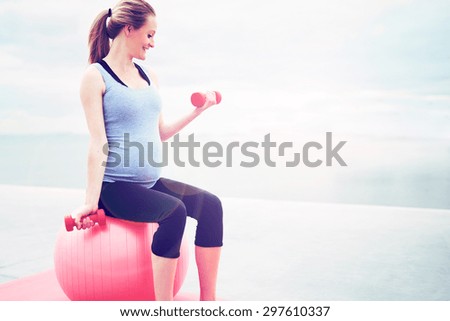 Pregnant woman doing fitness exercises sitting on a pilates gym ball working out with dumbbells, profile view with copyspace
