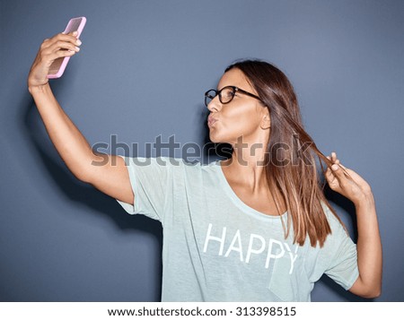 Young woman posing for a funny selfie as she puckers up her lips for a kiss in a teasing manner for the camera on her mobile phone