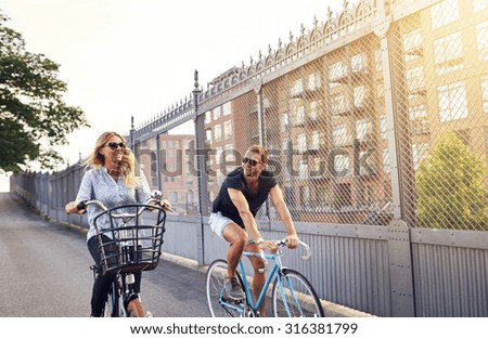 Young couple going for a summer bicycle ride cycling down an urban street past apartment blocks in their sunglasses smiling and chatting