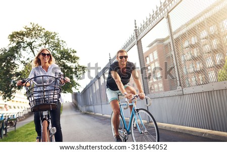 Young couple cycling in an urban park as they enjoy a healthy outdoor lifestyle in the fresh air and summer sun