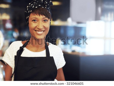 Successful young African American business owner standing in her coffee shop in an apron and bandanna smiling at the camera