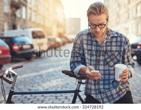 Outdoor portrait of modern young man with mobile phone in the street, sitting on bike
