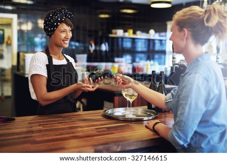 Customer in a pub paying the business owner or waitress with a credit card to be processed on a handheld banking machine, focus to the attractive African American owner
