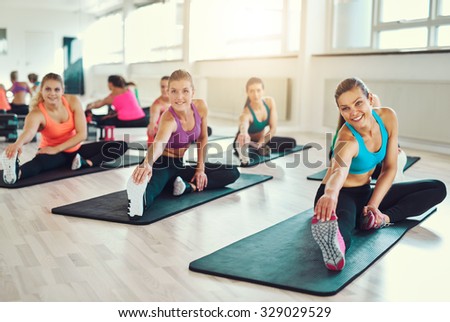 Group of young women in aerobics class at a gym doing stretching exercises to tone their muscles in a health and fitness concept