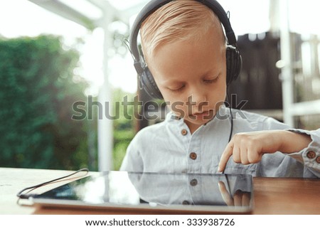 Pensive little boy selecting a new soundtrack from his music library on his tablet computer as he sits outdoors on a patio listening to music on stereo headphones