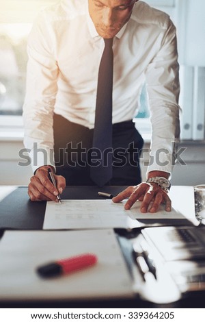 Business man closing a deal signing documents at desk in office wearing white shirt and tie