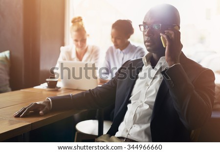 Black business man using cell phone, white and black business woman in background
