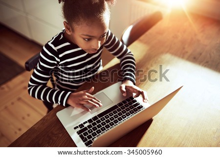 High angle view from above of a cute young African girl surfing the web on a laptop computer in an educational or recreational concept