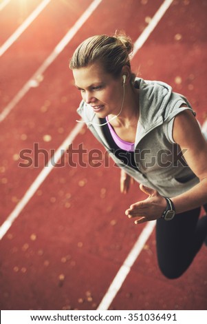 Close-up of athletic young sportswoman running fast on track field while listening to music
