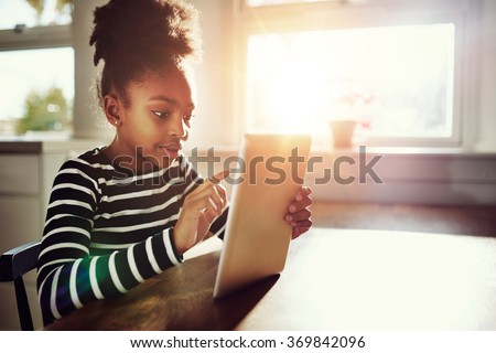 Young African-American Girl Surfing the Internet Using Tablet computer at the Table Inside Home.