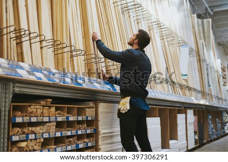 Carpenter selecting lengths of cut wood of a rack in a hardware store , low angle rear view from the side