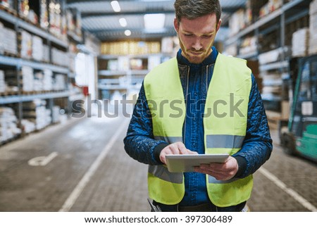 Young man looking up order details on a tablet as he shops in a hardware warehouse for supplies , close up upper body