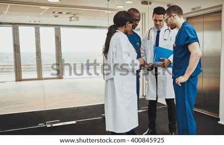 Diverse multiracial medical team consulting on a patient records standing in a foyer at a hospital grouped around a tablet computer