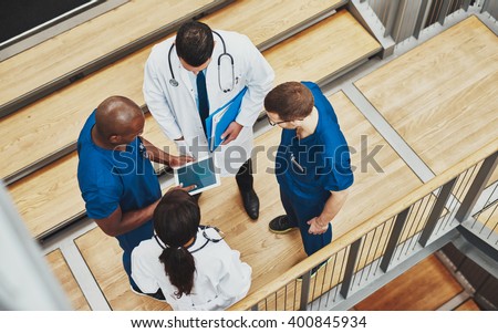 Multiracial medical team having a discussion as they stand grouped together around a tablet computer on a stair well, overhead view