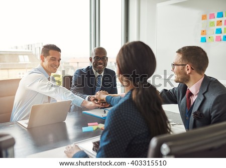 Successful multiracial business team working together affirm their commitment by linking hands across an office table during a meeting