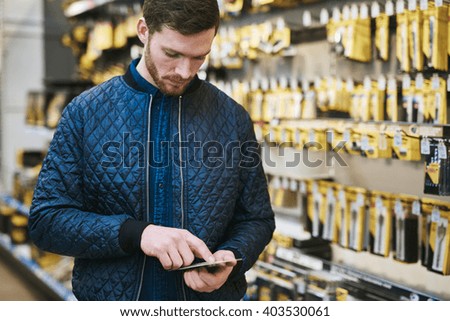 Young man checking a text message on his mobile phone as he shops in a hardware store store for DIY supplies