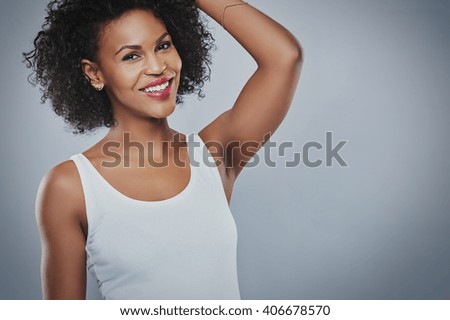 Single beautiful smiling African-American woman wearing sleeveless white undershirt with hand up toward head over gray copy space