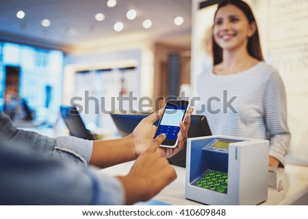 Close up view on fingers of customer entering information on phone in front of register as female cashier smiles in store