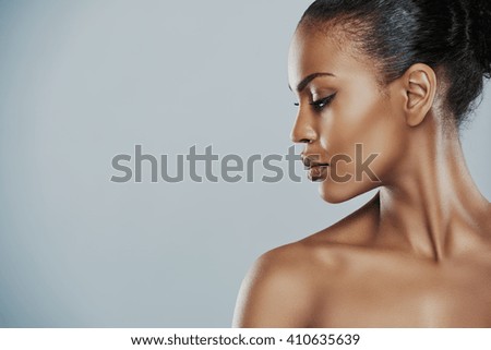 Profile view of beautiful grinning African bare shouldered female with short hair looking sideways over gray background