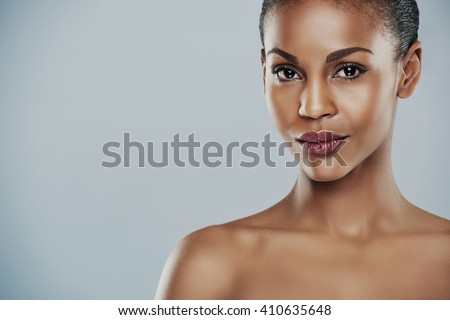Centered view of beautiful grinning African bare shouldered female with short hair and seductive expression and over gray background