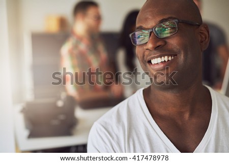 Close up of handsome smiling worker in white shirt and eyeglasses with three out of focus employees behind him in meeting