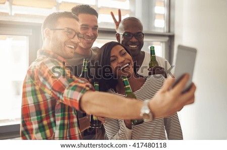 Friends at work taking self portrait with camera phone while holding green glass bottles of beer in office party