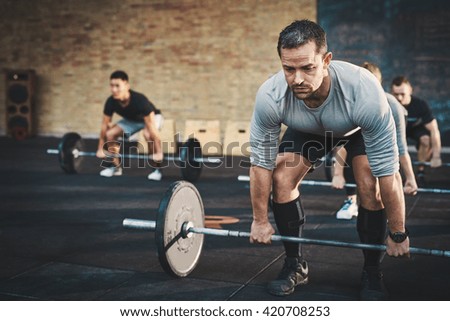 Fit young man lifting barbells looking focused, working out in a gym with other people
