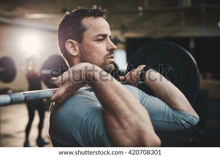 Fit young man lifting barbells looking focused, working out in a gym with other people