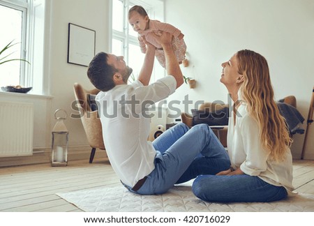 Proud father holding his newborn baby daughter in the air, with smiling mother sitting on the floor at home