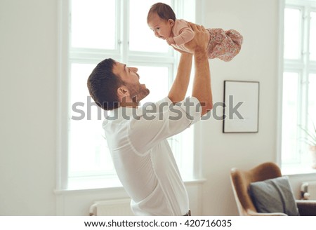 Proud father holding his newborn baby daughter up in the air at home