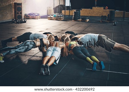 Fit young people focused on planking together in a circle in a gym
