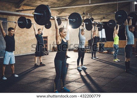 Fit young people lifting barbells looking focused, working out in a gym