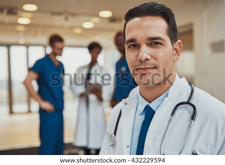 Male doctor with colleagues in background, doctor looking at camera with emergency team in background