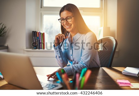 Smiling woman working at office using a laptop, warm colours sun light