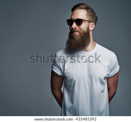 Portrait of handsome single bearded young man with serious expression wearing sunglasses and white short sleeve shirt looking over gray background with copy space