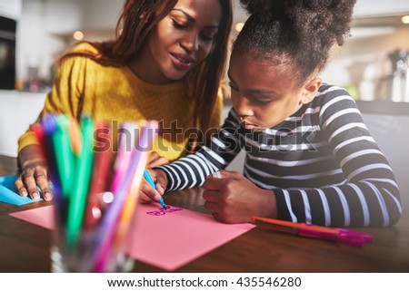 Mom and child drawing in kitchen, black mother and daughter