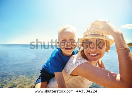 Happy young mother and son on a tropical beach with the laughing little boy getting a piggy back ride on her back