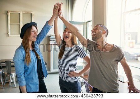 Laughing young business entrepreneurs in informal trendy clothing standing celebrating a success giving a high fives gesture