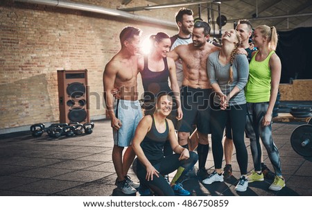 Group of eight happy muscular female and male adults standing together as good friends in gym with large speaker in background after a difficult workout session