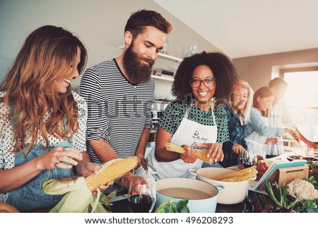 Happy group of young adult men and women cooking together at home in small kitchen or culinary classroom