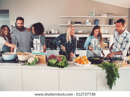 Six mixed Black and white friends preparing vegetables and pasta at long table in kitchen