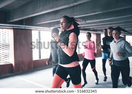 Attractive young urban runner pacing her team mates as she sprints through an undercover car park in a health and fitness concept