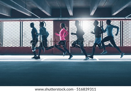 Group of diverse urban runners sprinting across the frame in an indoor car park as they workout backlit by the sun through a grid