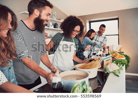 Large group of six happy friends preparing food for a pasta cooking class at table at home or in a small culinary school
