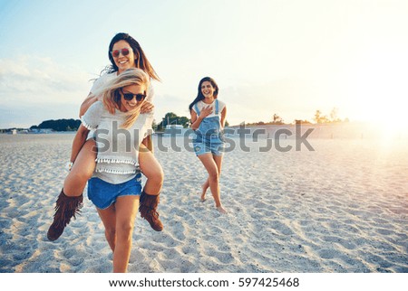Young cheerful girl giving her friend piggyback ride while third girl laughing at them.